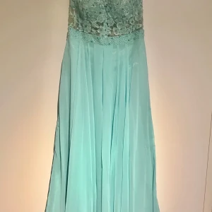 Balklänning med spetsdetaljer - Elegant mintgrön långklänning med vacker spets upptill och ett flödande kjolparti. Perfekt för speciella tillfällen med sin romantiska design.storlek M.