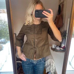 Olivgrön trekvartsärmad kappa  - Snygg olivgrön jacka med stora knappar framtill och trekvartsärmar. Jackan har en avslappnad passform och praktiska fickor. Perfekt för en stilren look.