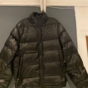 Svart pufferjacka, NIKE X NOCTA - Säljer en svart pufferjacka från NOCTA i samarbete med Nike. Jackan har en hög krage och dragkedja framtill. Svår att få tag på men nypris ligger runt 4000. Pris kan diskuteras