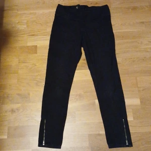 Svarta byxor med dragkedja från Pocket Money - Snygga svarta byxor från Pocket Money med dragkedja baktill och vid bensluten. Byxorna har en tight passform och är perfekta för en stilren look. De är tillverkade i ett bekvämt material som ger en skön känsla hela dagen.