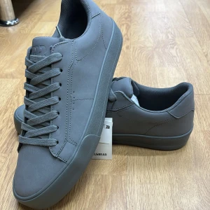 Grå sneakers från Pull&Bear - Snygga grå sneakers från Pull&Bear med klassisk design och snörning. Perfekta för en stilren look.