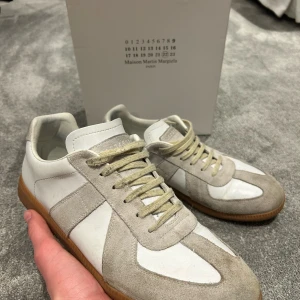 Maison Margiela gats - Snygga sneakers från Maison Martin Margiela i vitt och beige med snörning och gummisula. Perfekta för en stilren look.