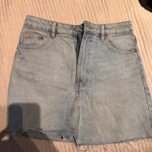 Jeanskjol från Zara - Säljer en snygg jeanskjol från Zara i ljusblå denim. Kjolen har en klassisk femficksdesign och rå kant nedtill för en trendig look. Perfekt för en avslappnad stil.