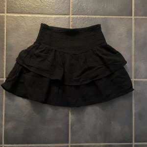 Svart kjol från Gina Tricot - Snygg svart kjol från Gina Tricot med volangdetaljer. Perfekt för en stilren look. Elastisk midja för bekväm passform.