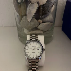 Silverfärgad klocka från Stuhrling - Snygg silverfärgad klocka från Stuhrling med vit urtavla . Klockan har en klassisk design med en robust länkarmband i metall. Perfekt för en stilren look. Hör av dig vid fler frågor eller ev bilder 😀