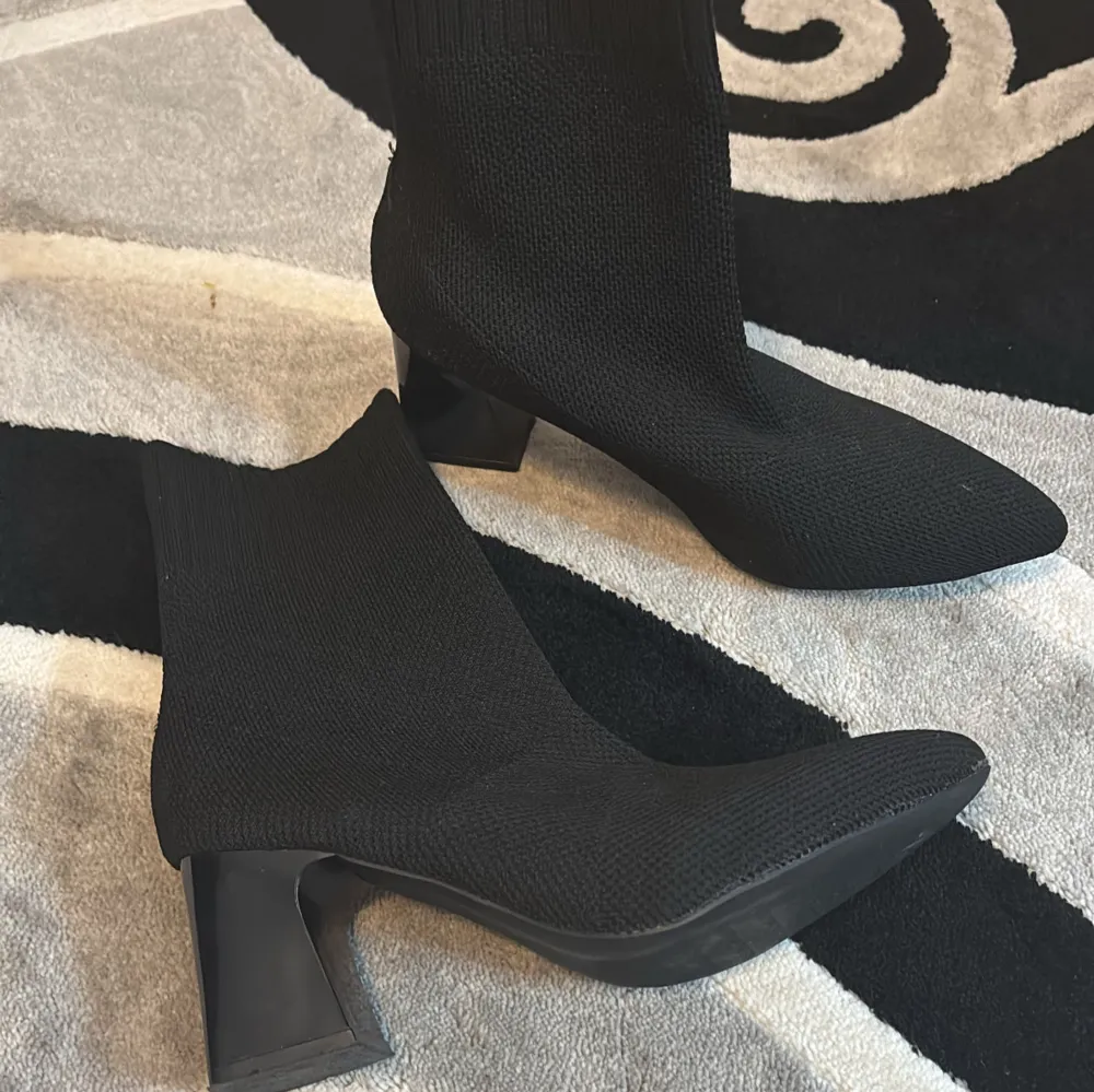 Snygga svarta stickade boots med spetsig tå och klack. Perfekta för en stilren look.. Kengät.