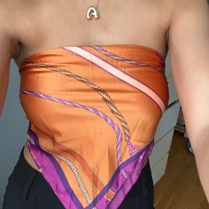 Orange och lila tubtopp - Trendig tubtopp i orange och lila med ett repmönster. Toppen är axelbandslös och knyts i ryggen, vilket ger en unik look. Perfekt för sommarens varma dagar. Det är egentligen en ”sjal” så du man kan använda den som sjal eller knyta den hur man vill och tycker om!! NYSKICK!