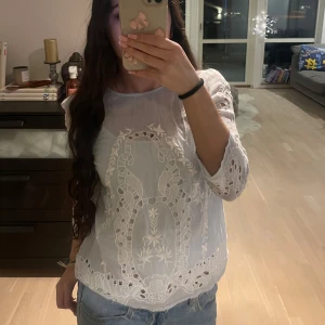 Vit blus med spetsdetaljer - Säljer en vacker vit blus med spetsdetaljer och broderier. Blusen har trekvartsärm och en rund halsringning. Perfekt för en elegant och stilren look.