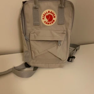 Beige ryggsäck från Fjällräven - Säljer en klassisk beige Fjällräven Kånken ryggsäck. Den har justerbara axelremmar, ett stort huvudfack och en mindre framficka med dragkedja. Perfekt för både vardag och äventyr. Ikonisk logga framtill.