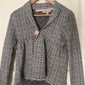 Mönstrad långärmad tröja från MyWear - Säljer en snygg långärmad tröja från MyWear med ett svartvitt mönster. Tröjan har en unik design med en knappdetalj framtill och en lätt volang vid midjan. Perfekt för höst och vår säsonger!