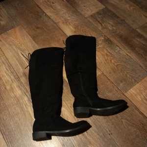 Svarta höga stövlar - Snygga svarta höga stövlar i mocka med snörning baktill. Perfekta för höst och vinter med en stilren design som passar till många olika outfits. Använt mycket sparsamt. 