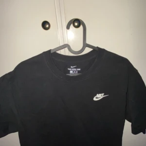 Svart t-shirt från Nike - Säljer en klassisk svart t-shirt från Nike med vit logga på bröstet. Perfekt för en sportig look eller avslappnad stil. T-shirten har en normal passform och är tillverkad i mjukt bomullsmaterial.