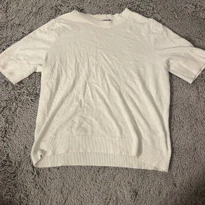 Vit kortärmad stickad tröja från 157 - Säljer en stilren vit tröja från 157 i storlek S. Tröjan är kortärmad och har en ribbad kant vid ärmslut och nederkant. Väldigt skönt material