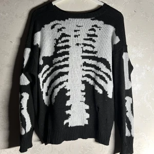 Svart stickad tröja med skelettmönster - Cool svart stickad tröja med ett  vitt skelettmönster på framsidan och ärmarna. Perfekt för en edgy look.