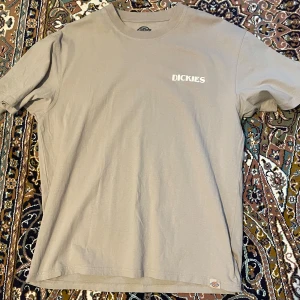 Grå t-shirt från Dickies - Snygg grå t-shirt från Dickies med tryck på både fram- och baksidan. Framsidan har en enkel logga medan baksidan har ett coolt blommönster och texten 'Plant Good Seeds & Keep Growing'. Perfekt för en avslappnad stil.