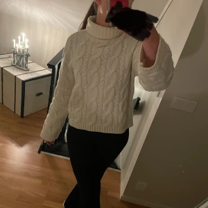 Vit stickad polotröja - Mysig vit stickad polotröja med kabelstickat mönster. Perfekt för kyliga dagar med sin höga krage och långa ärmar. En klassisk och stilren tröja som passar till det mesta.