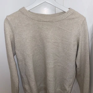 Beige stickad tröja från Vila - Säljer en stilren beige stickad tröja från Vila. Tröjan har en rund halsringning och långa ärmar, perfekt för kyligare dagar. Den är mjuk och bekväm, vilket gör den till ett mångsidigt tillskott i garderoben.