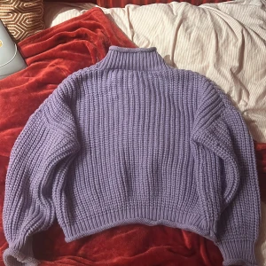 Lila stickad tröja - Mysig lila stickad tröja med hög krage och långa ärmar. Perfekt för kyliga dagar och ger en avslappnad look. Den ribbade strukturen ger extra stil och komfort.