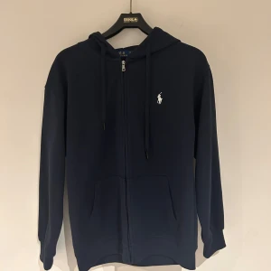 Mörkblå hoodie Polo Ralph Lauren - Snygg mörkblå hoodie från Polo Ralph Lauren med dragkedja och  logga på bröstet. Passar som en M. 