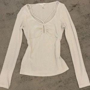 Vit ribbad topp från H&M - Säljer en stilren vit ribbad topp från H&M med långärmad design och v-ringad hals. Toppen har en snygg snörning framtill som ger en extra touch. Perfekt för både vardag och speciella tillfällen. knappt  använt . Den är i bra skickkkk