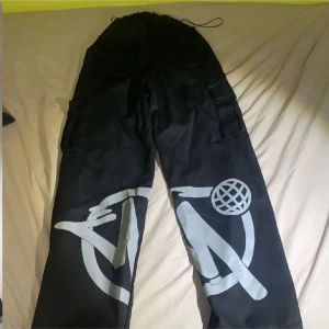 Svarta byxor med grafiskt tryck - Coola svarta byxor med stort grafiskt tryck i vitt. Byxorna har en loose passform och dragsko i midjan för justerbarhet. Perfekta för en avslappnad stil med en unik touch.