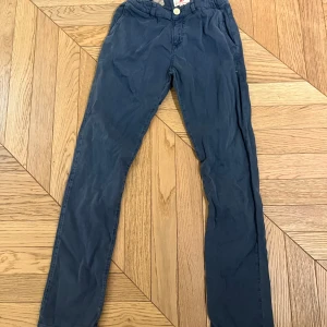 Blå byxor från American Outfitters - Säljer ett par blå byxor från American Outfitters. De har en knapp och dragkedja framtill samt justerbar midja för perfekt passform. Perfekta för en avslappnad stil.