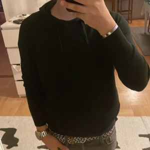 Svart hoodie - Säljer en stilren svart hoodie med långa ärmar. Perfekt för en avslappnad look. Den har en klassisk design med huva och ribbade muddar.