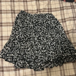 Svart blommig kjol från Amisu - Snygg svart kjol från Amisu New yorker med vita blommor. Kjolen har en volangdetalj och är kort i modellen. Perfekt för en trendig look! Inte använt många gånger, 4 gånger Max . 