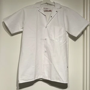 Vit kortärmad skjorta - Snygg vit kortärmad skjorta med knappar och en bröstficka. Perfekt för en stilren och avslappnad look.