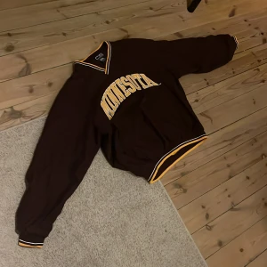 Vinröd baseball tröja från Crable Sportswear - Säljer en vinröd/mörk lila tröja från Crable Sportswear med texten 'Minnesota' i gult på bröstet. Tröjan har en v-ringad krage med gula och vita detaljer samt långa ärmar.