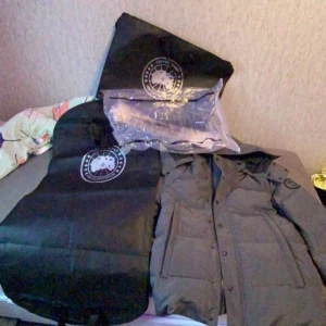 Svart parkajacka med huva och päls - Säljer en stilren svart parkajacka från Canada Goose. Jackan har en praktisk huva och flera fickor framtill. Perfekt för kyliga dagar. Plus päls med 