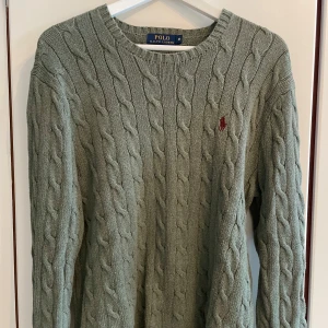 Grön stickad tröja från Ralph Lauren - Säljer en stilren grön stickad tröja från Ralph Lauren med kabelstickat mönster. Tröjan har en broderad röd logotyp på bröstet och rund halsringning. Strl M. Lite nopprig. Hör av dig om du har några frågor.
