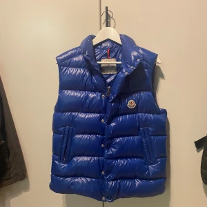 Moncler Vest modell Tibb - En mörkblå moncler vest i otroligt bra skick, näst intill helt ny 10/10 då den används enbart vid väldigt få tillfällen. den är av modellen Tibb som är tjockare än gui. Den är köpt på NK i Stockholm, januari detta år. 