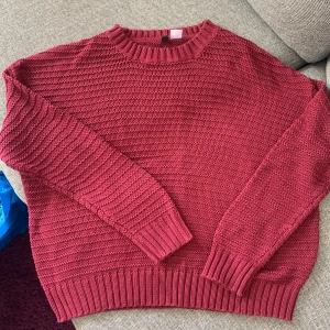Röd stickad tröja - Säljer en supermysig stickad tröja som är perfekt för kyliga dagar. Den har en klassisk rund hals och långa ärmar med ribbade muddar. Perfekt för höst och vinter! Något kortare modell. 