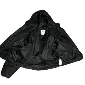 Svart pufferjacka från Nike - Säljer en svart pufferjacka från Nike. Den är perfekt för kalla dagar med sin vadderade design och har en praktisk huva. Jackan har en dragkedja framtill och är i ett snyggt, quiltat mönster. Den är både stilren och funktionell, perfekt för vintern!