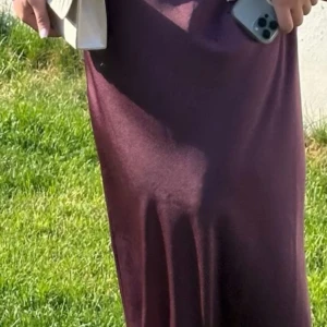 Mörk vinröd långklänning - Säljer en elegant mörk vinröd långklänning. Klänningen har en tight passform och är långärmad, är endast använd en gång för bal!  Materialet ser ut att vara mjukt och bekvämt, vilket gör den idealisk för både fest och mer formella tillfällen. 