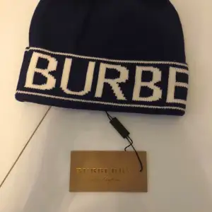 Säljer en snygg blå mössa från Burberry med deras ikoniska logga i vitt. Mössan är perfekt för att hålla sig varm och stilren under kyliga dagar. Den är i nyskick och kommer med etikett. Passar perfekt till både vardag och lite finare tillfällen.