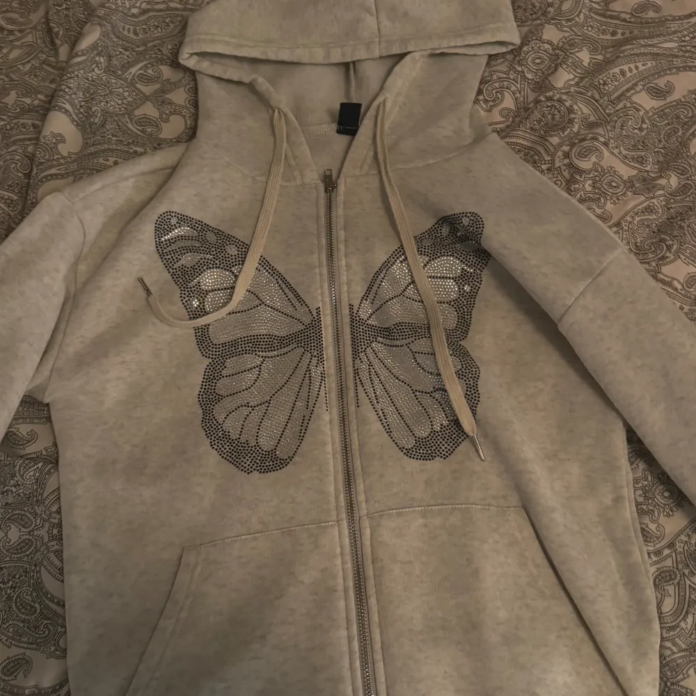 Hoodie med dragkedja från Shein. Storlek XS. En fjäril i pärlor på framsidan. Super mjuk och skön, ej använd många gånger. Tar bara Swish, skriv till mig vid intresse 💌. Hoodies.