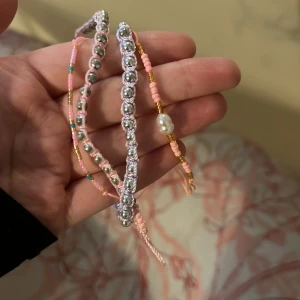 Färgglada armband med pärlor - Säljer ett set med tre handgjorda armband. Ett armband har silverpärlor, ett har rosa och guldpärlor med en stor vit pärla, och det tredje har små färgglada pärlor. Perfekt för att ge en färgklick till din outfit! 25kr st