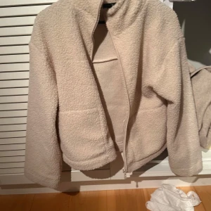 Beige teddyjacka från new yorker  - Mysig beige teddyjacka från new yorker med dragkedja framtill. Perfekt för kyliga dagar med sin fluffiga och varma design. Jackan har en enkel och stilren look som passar till många olika outfits.