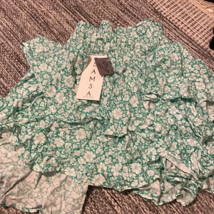 Blommig kjol från Jamsa - Söt blommig kjol i grönt och vitt från Jamsa. Kjolen har volanger och en elastisk midja för bekväm passform. Perfekt för en somrig look! Inte använd!! Prislapp kvar! Den är grön/turkos 