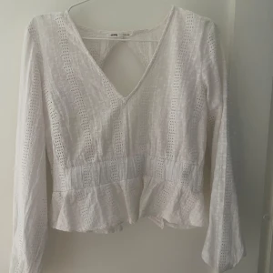 Vit blus från Sinsay - Säljer en söt vit blus från Sinsay med v-ringning och öppen rygg. Blusen har långa ärmar och är dekorerad med spetsdetaljer. Perfekt för en stilren look.