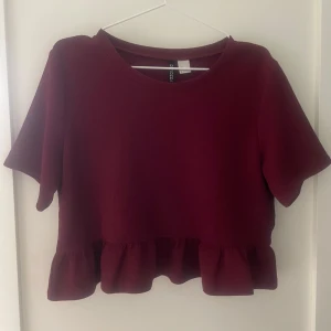 Vinröd topp från H&M - Säljer en vinröd topp från H&M med korta ärmar och volangdetalj vid nederkanten. Toppen är i bra skick och har bara används några gånger, jag säljer den alltså då den inte används. Skriv om du har några frågor❤️❤️