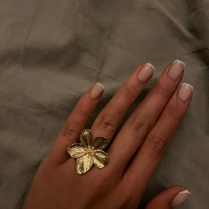 Guldfärgad blomring - Justerbar, Elegant guldfärgad ring formad som en blomma med detaljerade blad. Perfekt för att ge en touch av naturinspirerad stil till din look.