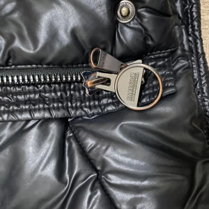 Svart pufferjacka från Barbour - Snygg svart pufferjacka från Barbour International med quiltad design och dragkedja. Jackan har en mjuk insida och stilrena detaljer som ger en exklusiv känsla. Perfekt för kyligare dagar. I nyskick o inga skador !