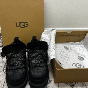 Uggs lowmel - Säljer ett par svarta boots från UGG med snörning och pälsdetaljer. Skorna har en robust sula och är perfekta för kyligare väder. De kommer i originalkartong.