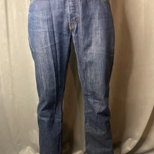 Blå Levis 501 jeans - Klassiska blå Levis 501 jeans med rak passform. Tillverkade i slitstarkt denim med knappgylf och femficksdesign. Perfekta för en avslappnad stil.