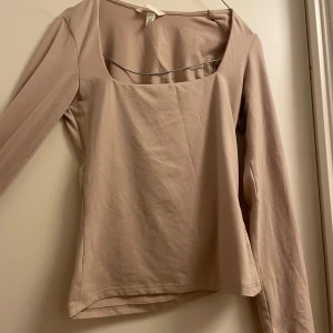Beige långärmad topp från H&M - Säljer en stilren beige långärmad topp från H&M. Toppen har en fyrkantig urringning och är tillverkad i ett mjukt material som ger en bekväm passform. Perfekt för både vardag och mer uppklädda tillfällen.