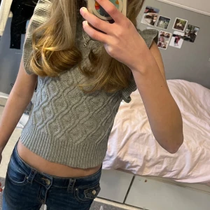 Grå stickad topp från Shein 💓 - Säljer en grå stickad topp från Shein med ett snyggt flätmönster. Toppen är ärmlös med volangdetaljer vid axlarna och har en ribbad kant vid midjan. Tröjan säljs billigt och vill gärna ha snabb affär 🫶🏻 - Priset kan diskuteras