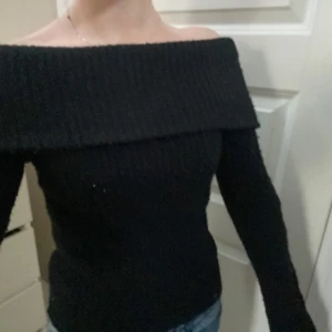 Svart offshoulder stickad tröja - Snygg svart offshoulder tröja i stickat material. Perfekt för en stilren look med långa ärmar och en bred krage som ger en elegant touch. Passar bra till både jeans och kjol. Fint skick men tyvärr lite nopprig som man ser på bilderna.💕💕